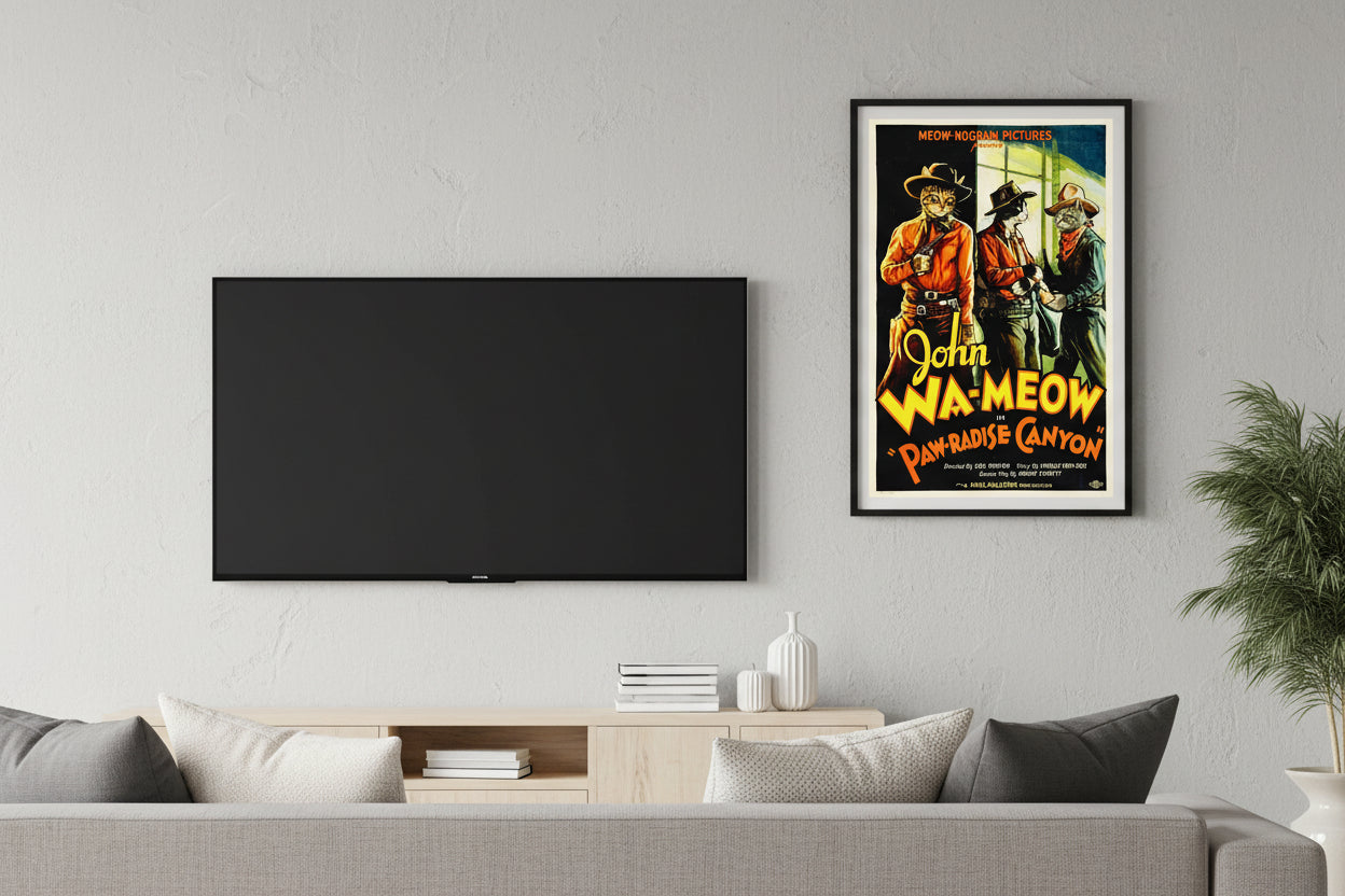 Vintage Western movie poster parody titled 'John Wa-meow in Paw-radise Canyon' featuring a ginger tabby cat dressed as a cowboy with a hat and holster, standing alongside two other cowboy cats against a scenic canyon backdrop. Based on the movie by John Wayne. Hung over a white table and Books near a fern.