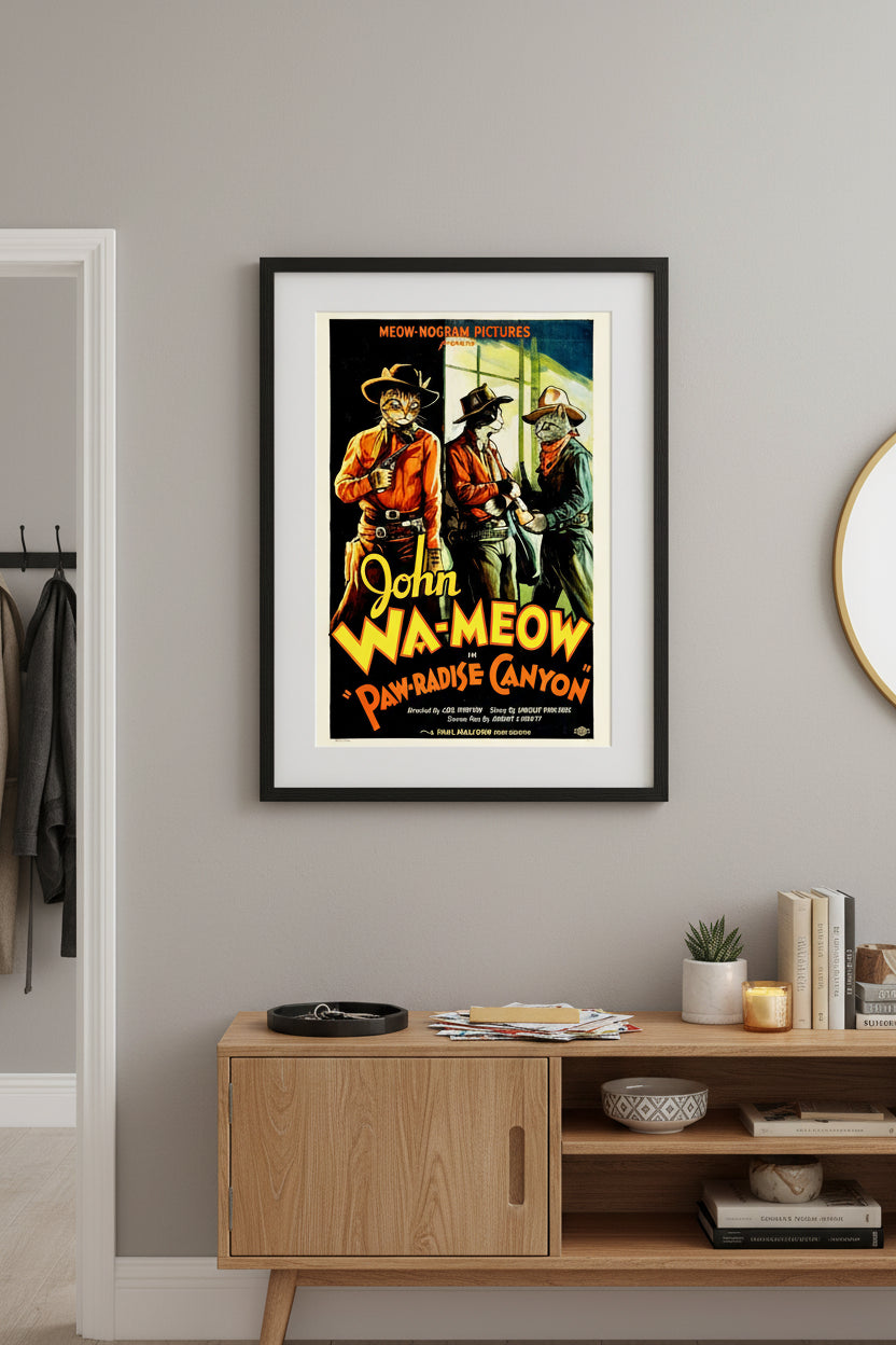 Vintage Western movie poster parody titled 'John Wa-meow in Paw-radise Canyon' featuring a ginger tabby cat dressed as a cowboy with a hat and holster, standing alongside two other cowboy cats against a scenic canyon backdrop. Based on the movie by John Wayne. Hung near a cluttered credenza.